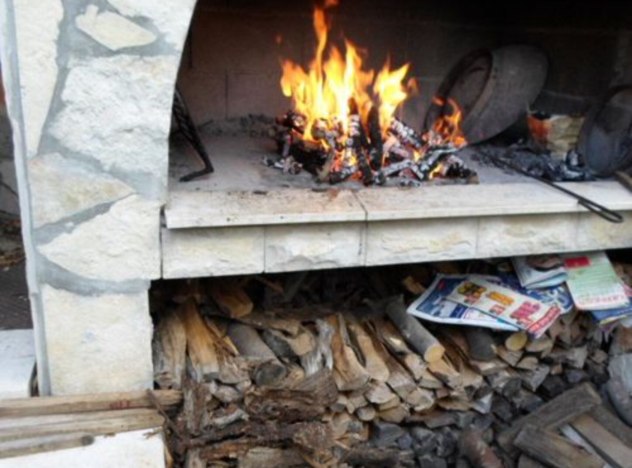 A stone fireplace with a fire burning inside, surrounded by logs and newspapers.