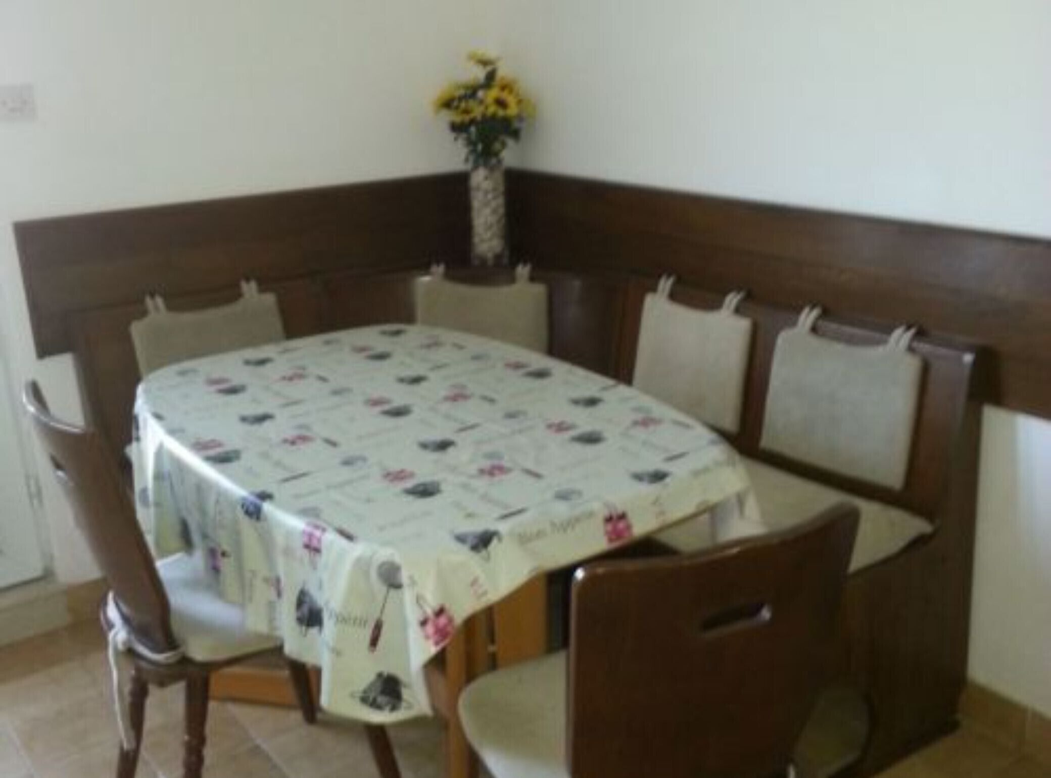 Un área de comedor con una mesa redonda cubierta por un mantel floral, rodeada de sillas de madera con asientos acolchados.