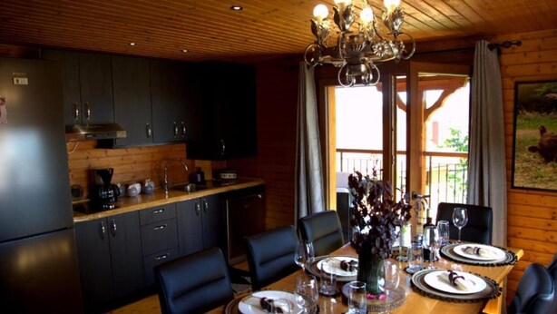 A wooden interior with a dining table set for four, a kitchen with dark cabinets, and a chandelier. - Brezova Poljana Lodge with Sauna and Hot-Tub - Five Bedroom Holiday Home (Vrbovsko)