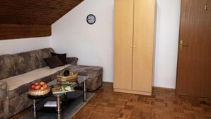 Una sala de estar acogedora con techo de madera, un sofá, una mesa de centro con frutas y un armario.