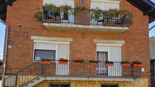 Un edificio de dos pisos con fachada de ladrillo, contraventanas blancas y un balcón con jardineras.