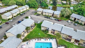 Vista aérea de una zona residencial con piscina rodeada de casas, un estacionamiento y una masa de agua.