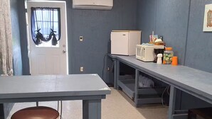 A room with a kitchenette, a small table with a stool, and a door with a window.