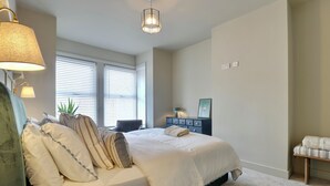 Ein Schlafzimmer mit Bett, Nachttischen, einem Schminktisch und einem Fenster mit Jalousien.