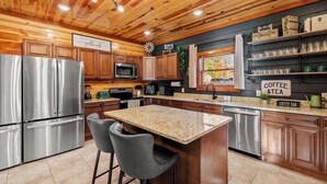 A modern kitchen with stainless steel appliances, wooden cabinets, and a granite countertop. - Amazing Luxury NEW 8bdrm Cabin-Pool-Arcades-Gazebo (Sevierville)