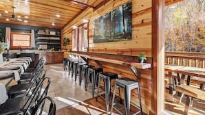 A wooden interior with a bar area, seating, and a large forest painting. - Amazing Luxury NEW 8bdrm Cabin-Pool-Arcades-Gazebo (Sevierville)