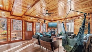 A cozy cabin interior with wooden walls, a hammock, and a fireplace. - Amazing Luxury NEW 8bdrm Cabin-Pool-Arcades-Gazebo (Sevierville)