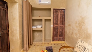 A room with a wooden door, a beige wall, a wooden cabinet, a small table with fruit, a patterned sofa, and a patterned rug. - Riad Lalla Fatima  (Marrakech)