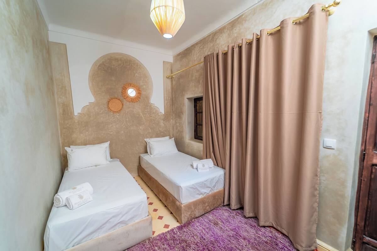 Ein Zimmer mit zwei Einzelbetten, einem violetten Teppich, einer Wanduhr und einem Fenster mit Vorhängen.