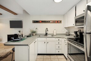 Eine moderne Küche mit weißen Schränken, einem Edelstahlkühlschrank, einem eingebauten Ofen und einem Flachbildfernseher an der Wand.