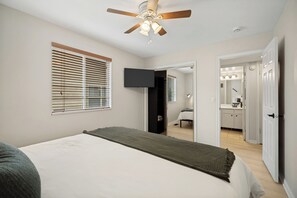 A bedroom with a bed, a ceiling fan, a TV, and a bathroom visible through an open door. - 1BD King Condo – Walking Distance to PCMR on Park Ave (Park City)