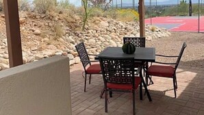An outdoor patio with a table and chairs, a basketball court in the background, and a desert landscape.