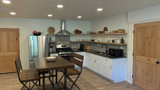 A modern kitchen with white cabinets, a stainless steel refrigerator, a wooden dining table with chairs, and a black microwave.