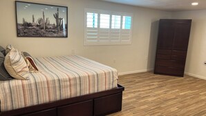 A bedroom with a bed, a window with blinds, a dark wardrobe, and a wall-mounted picture.