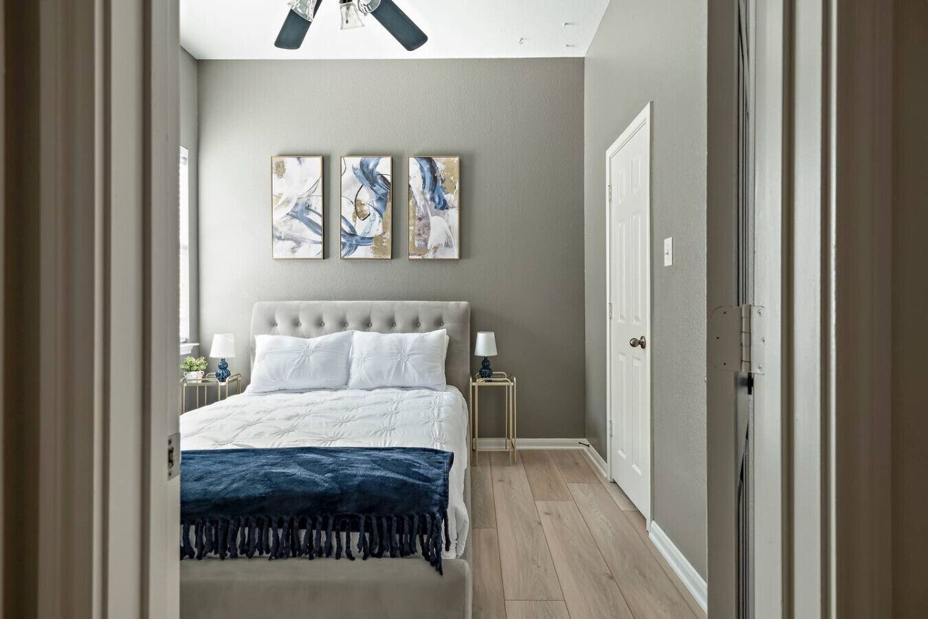 A bedroom with a bed, a ceiling fan, and three wall-mounted paintings.