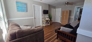 A living room with a brown sofa, a wooden bench, a television, and a ceiling fan. - Waterfront, Private dock for 4 boats, Sleeps 13+, Fire Pit, Movie Projector. (Old Town)