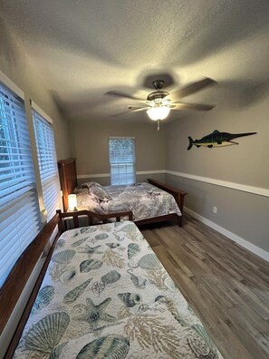 Ein Schlafzimmer mit zwei Betten, einem Deckenventilator, einer Wanddekoration mit Fischen und einem Fenster mit Jalousien.