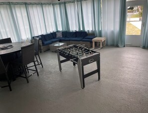 Quarto com mesa de futebol, mesa redonda com cadeiras, sofá e pequena mesa.