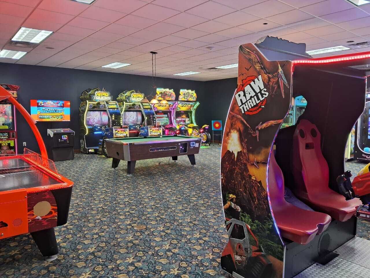 An indoor arcade with various gaming machines, a pool table, and a racing game setup.