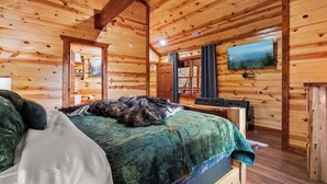 Ein gemütliches Schlafzimmer einer Holzhütte mit einem Bett, einem Fernseher und einer Tür zu einem weiteren Raum.