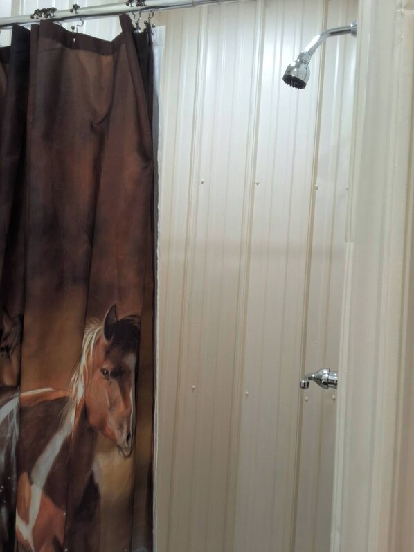 A bathroom with a shower curtain featuring a horse, a white door, and a showerhead.