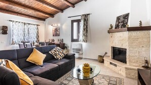 A living room with a fireplace, a sofa, a coffee table, and a dining area with a table and chairs. - Rifugio Del Sole Villa con Piscina (Noto)