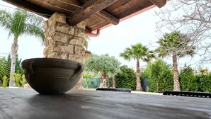 A stone pillar under a wooden roof structure, with a bowl on a table in the foreground. - Rifugio Del Sole Villa con Piscina (Noto)