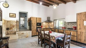 A kitchen with wooden cabinets, a dining table with chairs, a built-in oven, and a hanging light fixture. - Rifugio Del Sole Villa con Piscina (Noto)