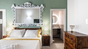 A bedroom with a large ornate mirror, a bed with white and gold bedding, a wooden dresser, and a nightstand with a lamp. - Rifugio Del Sole Villa con Piscina (Noto)