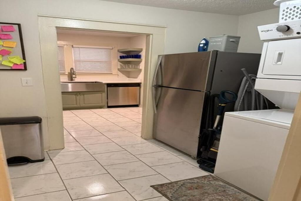 A kitchen with a stainless steel refrigerator, a washing machine, and a trash bin.