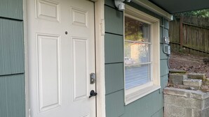 A white door with a keypad lock, a window with a closed shutter, and a small outdoor area with a wooden fence and steps leading up to a house. - South Seattle, Free Parking, Private Entrance and 3/4 Bath, Q Bed, Free Laundry. (Seattle)
