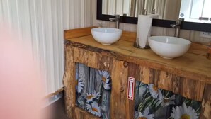 A bathroom with a wooden vanity, two white ceramic sinks, a mirror, and a fire safety sign. - Morgan Cabin (Heavener)