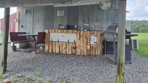 An outdoor barbecue area with a wooden counter, grill, and seating. - Morgan Cabin (Heavener)