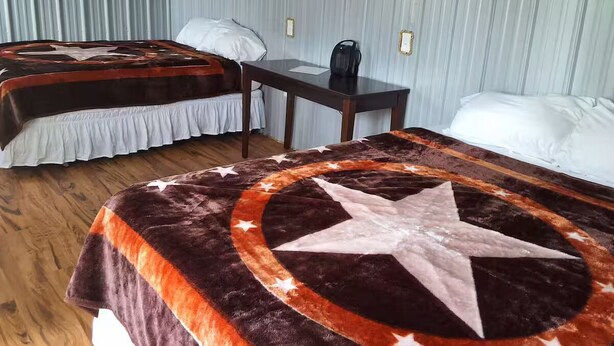 A room with two beds, each with a distinct blanket design, a small table with a telephone, and a wall-mounted electrical outlet. - Morgan Cabin (Heavener)