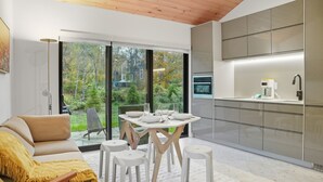Cuina moderna amb una finestra gran, zona de menjador amb tamborets i un sofà amb una manta groga.