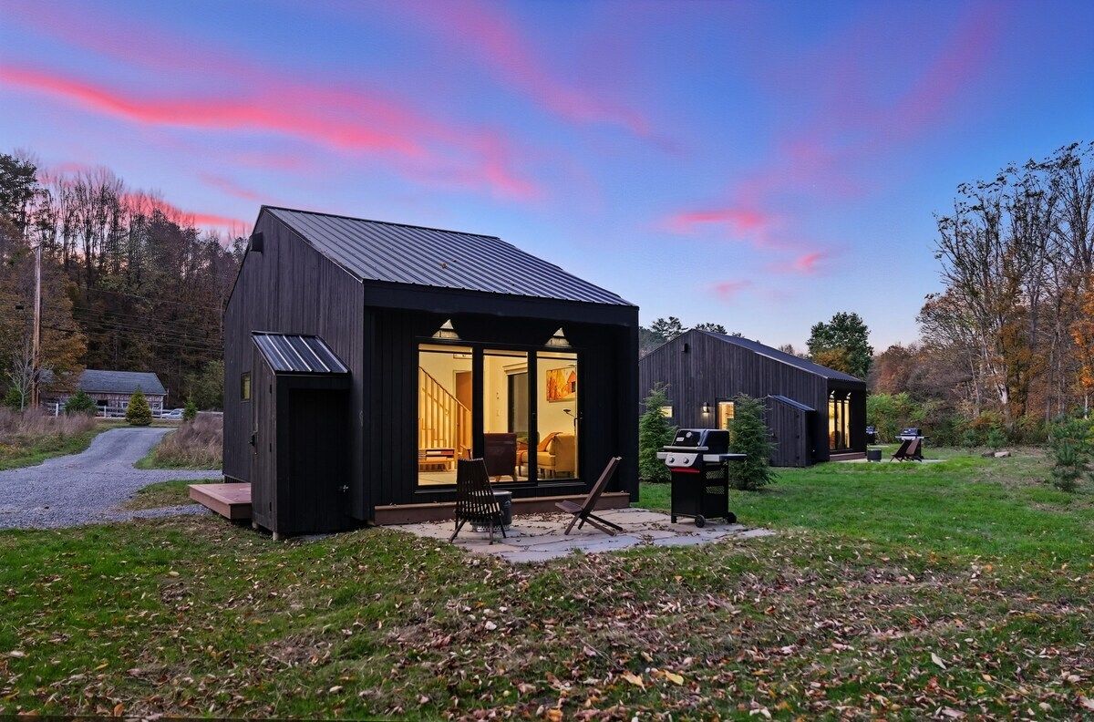 Un moderno chalet con un'ampia porta vetrata, un patio con posti a sedere all'aperto e un barbecue.