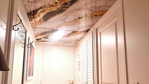 Een hal met een betegelde vloer, witte deuren en een plafond met een decoratief patroon.