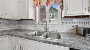 A kitchen with white cabinets, a double sink, a window with a floral curtain, and a toaster on the counter. - Four Seasons Haven (Angola)