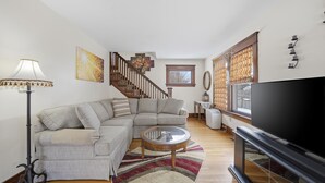 A living room with a sectional sofa, a glass coffee table, a flat-screen TV, a floor lamp, and a staircase. - Four Seasons Haven (Angola)