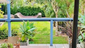 Un porche cubierto con una mesa y sillas de madera, rodeado de plantas en macetas y vistas a un jardín exuberante.