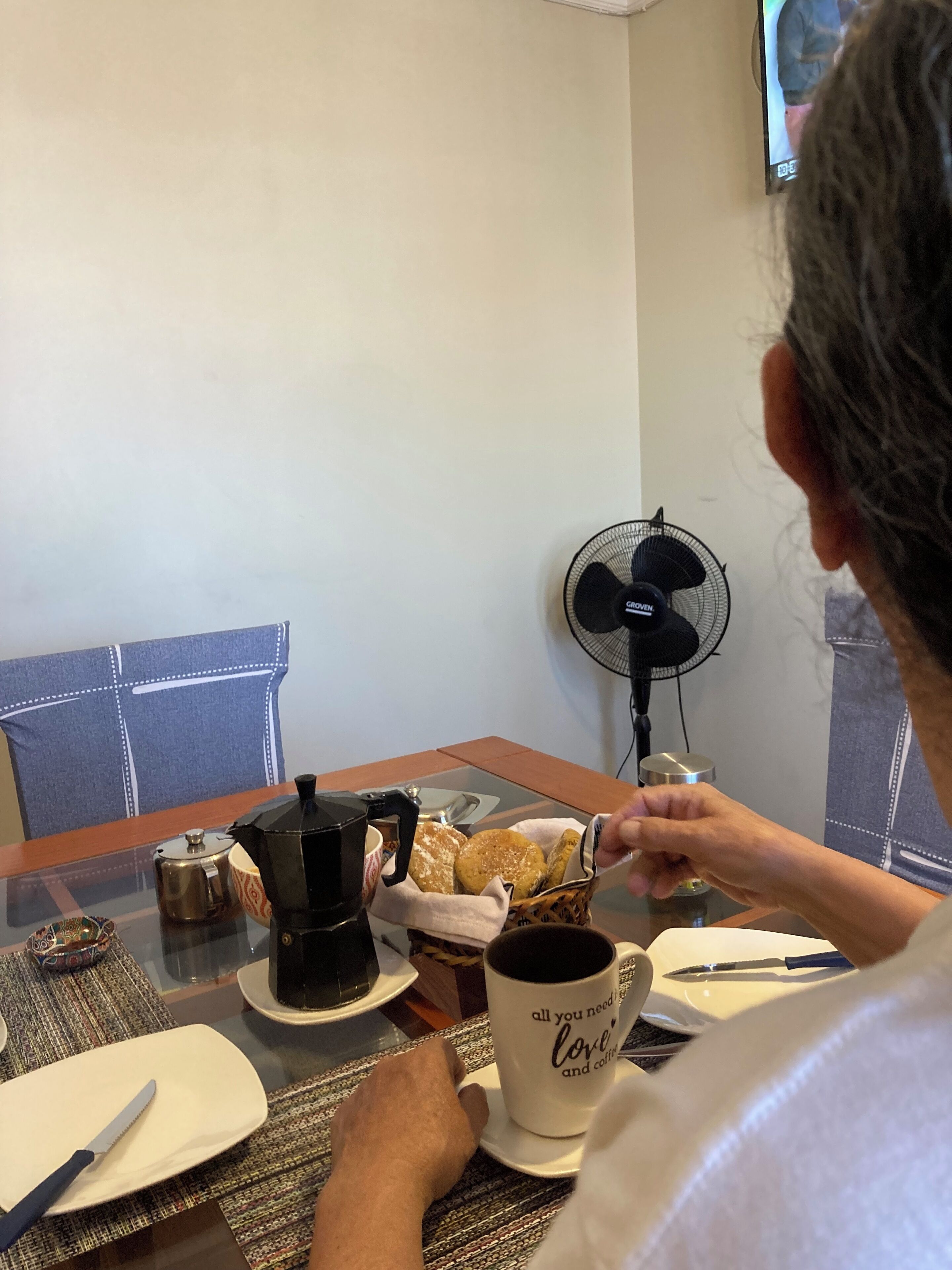 Iemand zit aan een tafel met een koffiezetapparaat, een mok en een mand gebak.