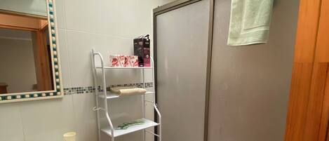 A bathroom with a toilet, sink, mirror, and shelves.