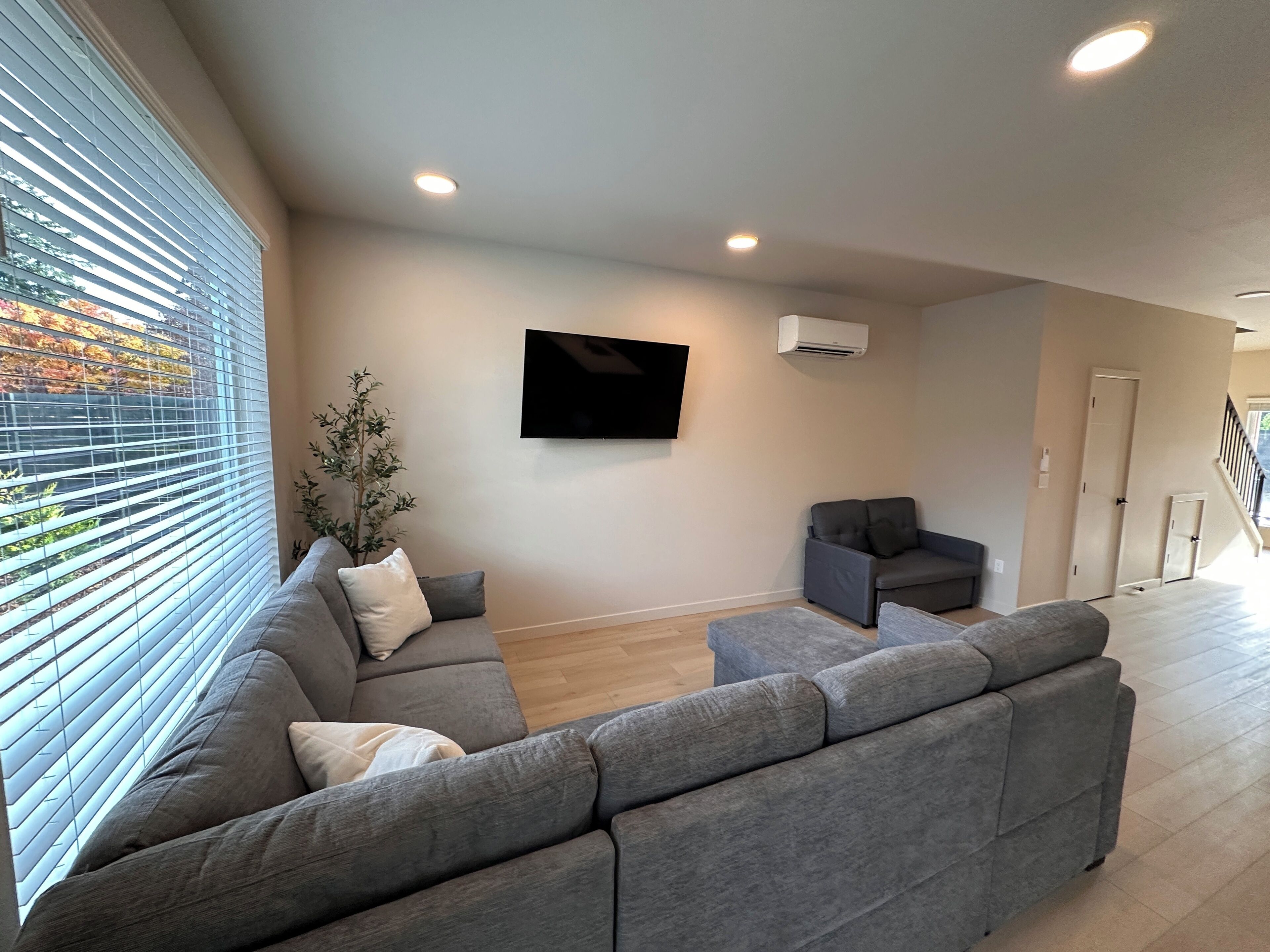 Una sala de estar moderna con un sofá seccional gris, un sillón gris pequeño y un televisor de pantalla plana montado en la pared.