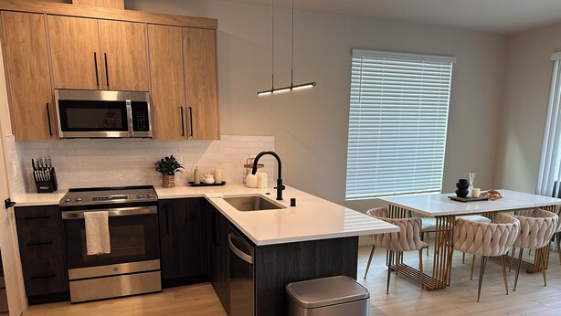 Une cuisine moderne avec des meubles en bois, des appareils en acier inoxydable, un îlot central doté d’un évier et un coin repas avec une table et des chaises.