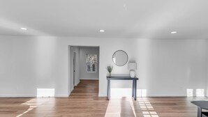 A spacious room with wooden flooring, a console table with a mirror and lamp, and a staircase leading to another area. - Tennessee Tranquility • Fire Pit • Forest Views (Ashland City)