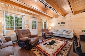 A log cabin interior with a fireplace, leather chairs, a sofa, and a large rug. - Lazy Dawg Cabin| 30min to Yellowstone, Pet Friendly, Fire Pit! (Island Park)