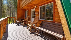 Una cabaña de madera con terraza, mecedoras y un banco.