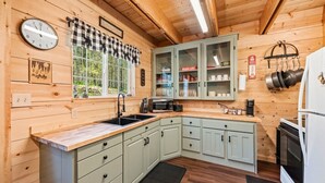 Una cocina con paredes de madera, un valance de ventana a cuadros, un reloj y armarios con puertas de cristal.