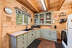 A kitchen with wooden walls, a checkered window valance, a clock, and cabinets with glass doors.