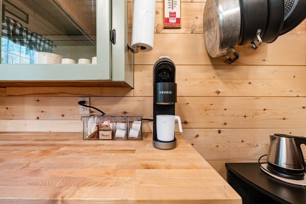 A kitchen with a Keurig coffee maker, a coffee mug, a kettle, and a clear plastic container with coffee pods.
